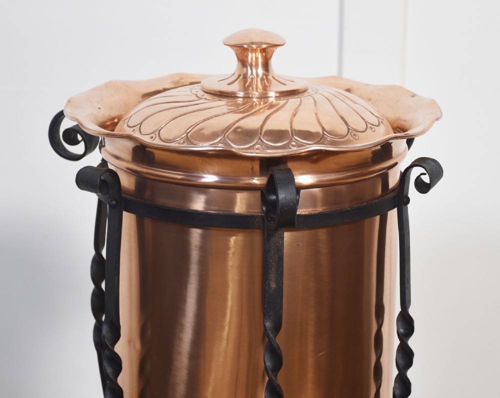 An Arts and Crafts circular copper coal bucket with a fluted lid, supported within a black wrought iron frame with twisted uprights and scroll legs. View III
