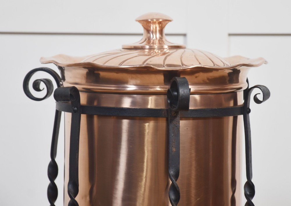 An Arts and Crafts circular copper coal bucket with a fluted lid, supported within a black wrought iron frame with twisted uprights and scroll legs. View V