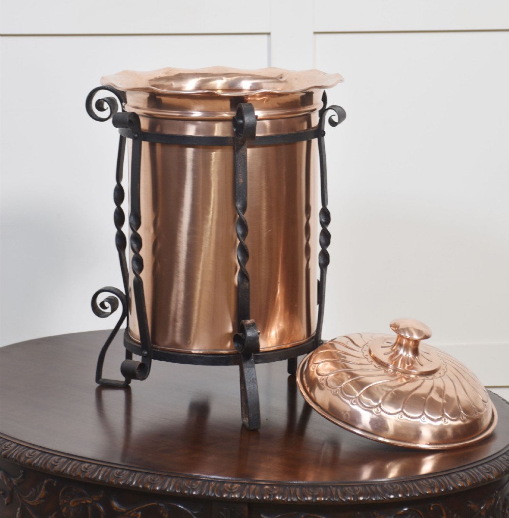An Arts and Crafts circular copper coal bucket with a fluted lid, supported within a black wrought iron frame with twisted uprights and scroll legs. View VII