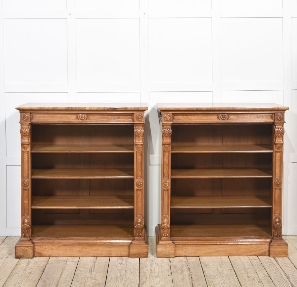 A pair of 19th-century walnut open bookcases featuring carved pilasters, rosette details, adjustable shelves, and heavy plinth bases.