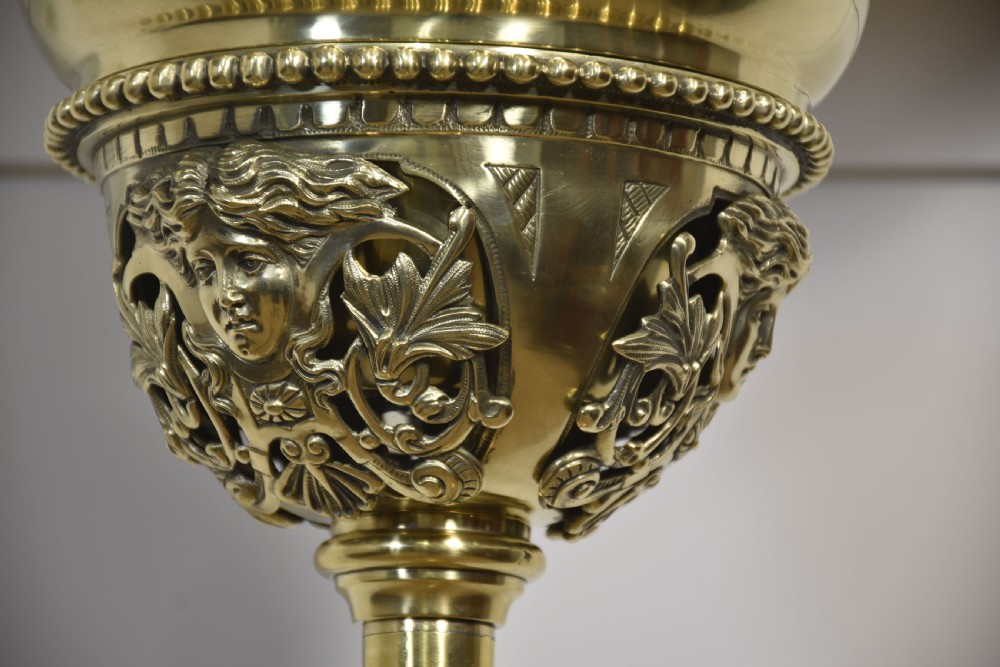A tall Victorian polished brass standard lamp featuring a fluted column, Corinthian capital, a decorative urn reservoir, and a stepped square base adorned with laurel wreath motifs. View X