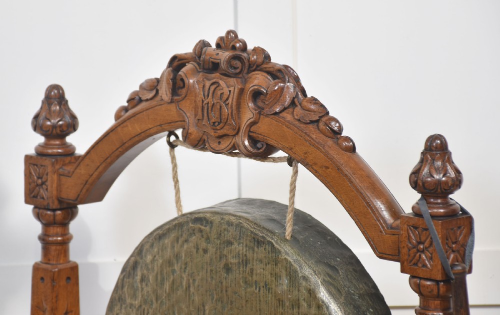 A freestanding carved oak frame featuring turned posts, scroll feet, and a central suspended round brass gong with an attached striker. View V