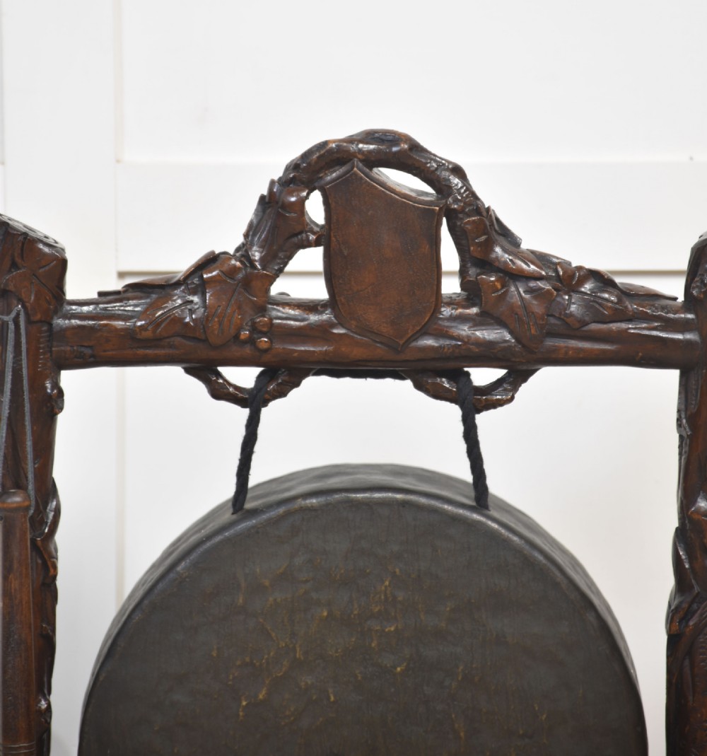 A dark carved oak frame styled with rustic branch motifs holding a central suspended metal circular gong and mallet. View V