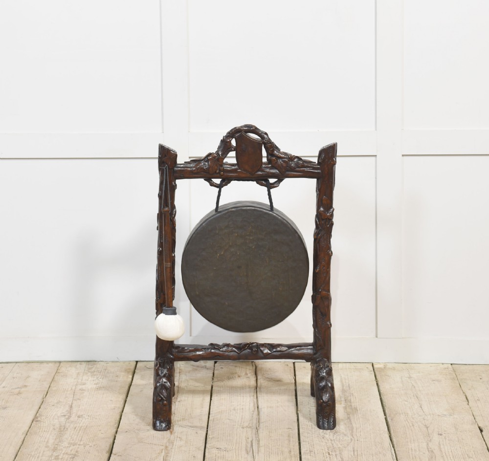 A dark carved oak frame styled with rustic branch motifs holding a central suspended metal circular gong and mallet. View VI