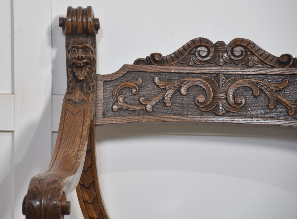 A carved oak double curule bench featuring scrolled armrests, carved mask details, and a slatted seat. View II