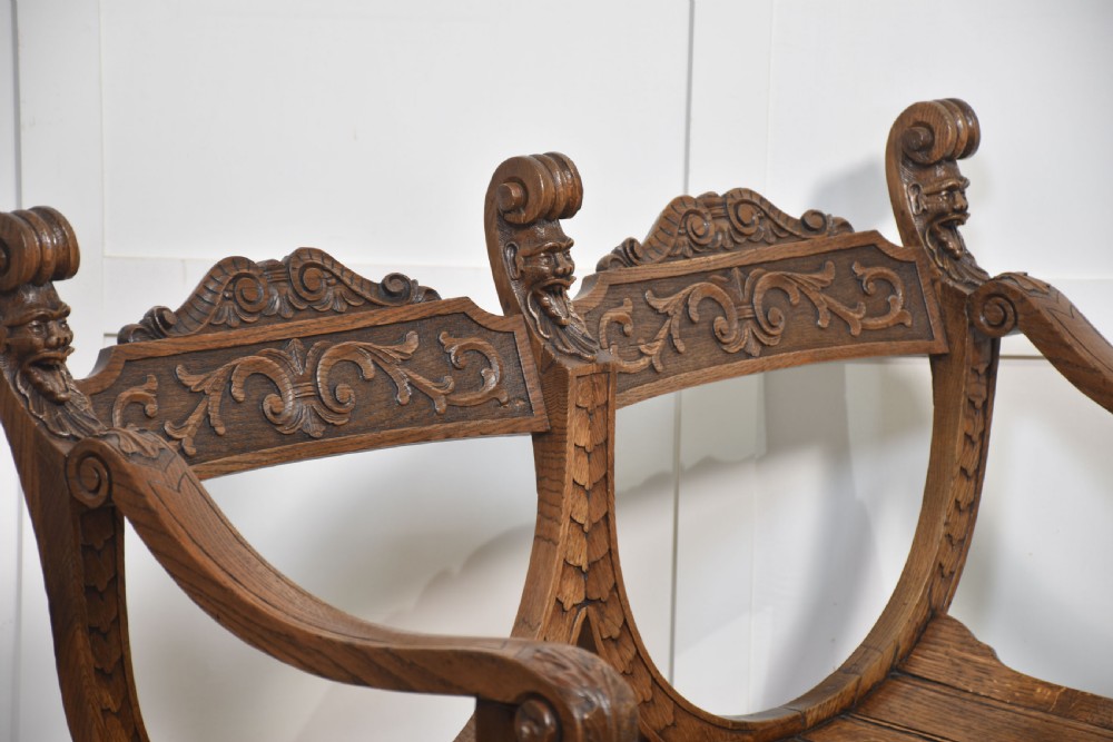 A carved oak double curule bench featuring scrolled armrests, carved mask details, and a slatted seat. View III