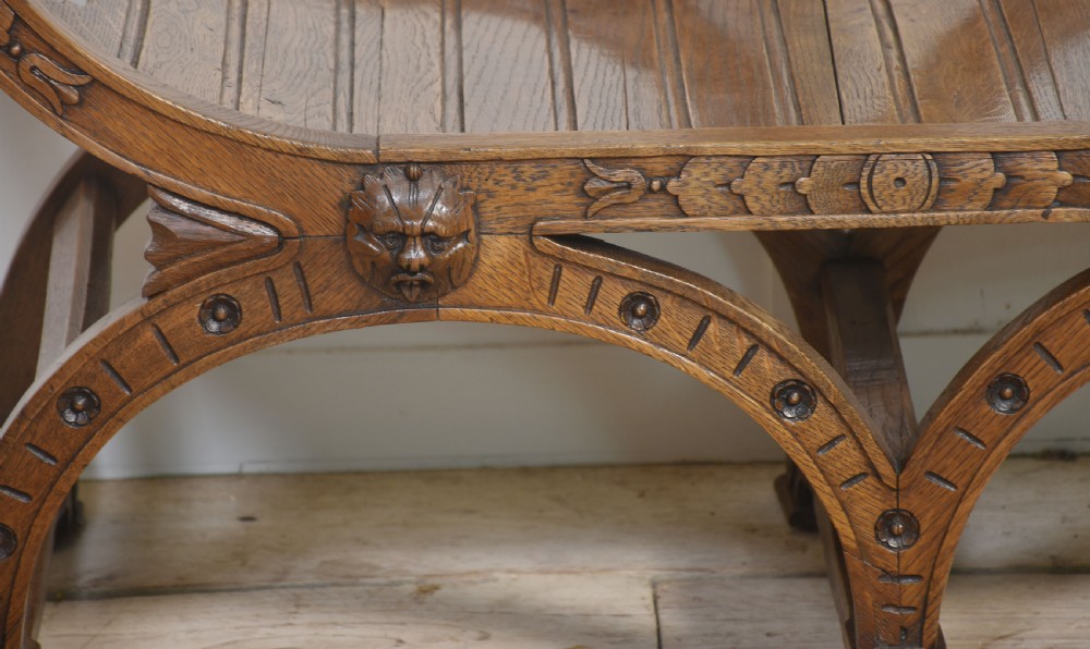 A carved oak double curule bench featuring scrolled armrests, carved mask details, and a slatted seat. View V