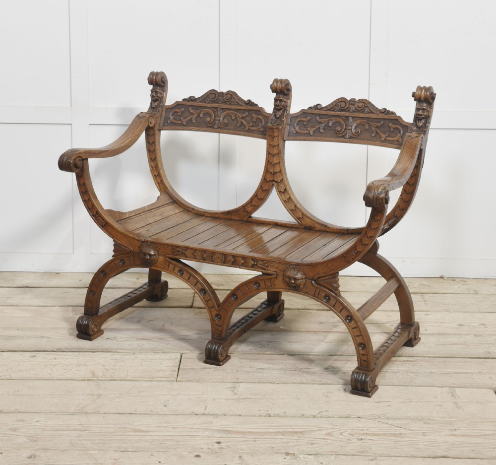 A carved oak double curule bench featuring scrolled armrests, carved mask details, and a slatted seat. View VIII