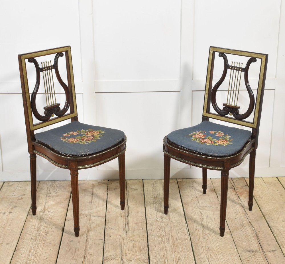A pair of antique mahogany side chairs featuring open lyre-shaped backrests with brass accents and blue fabric seats upholstered with floral tapestry.