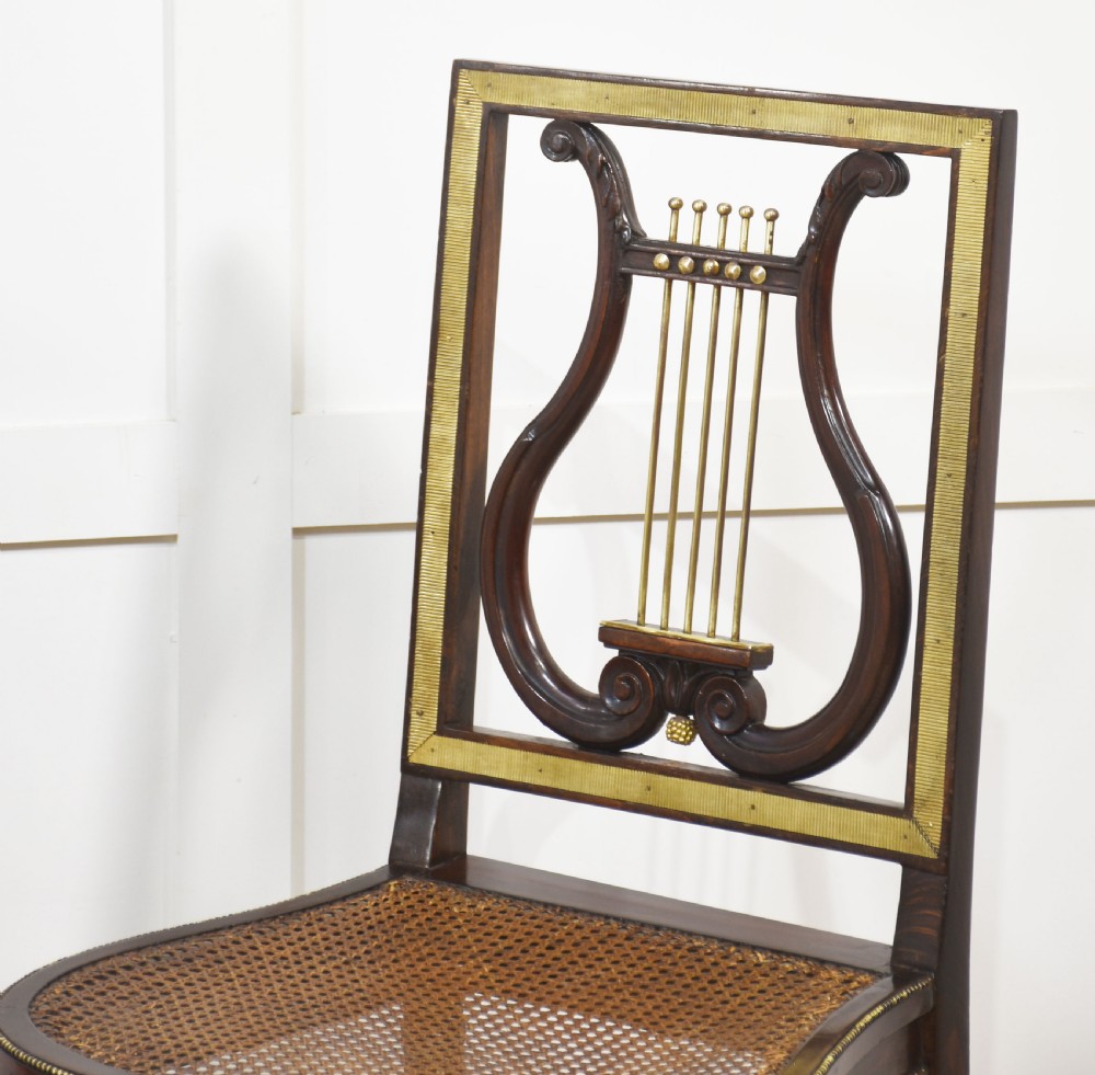 A pair of antique mahogany side chairs featuring open lyre-shaped backrests with brass accents and blue fabric seats upholstered with floral tapestry. View V