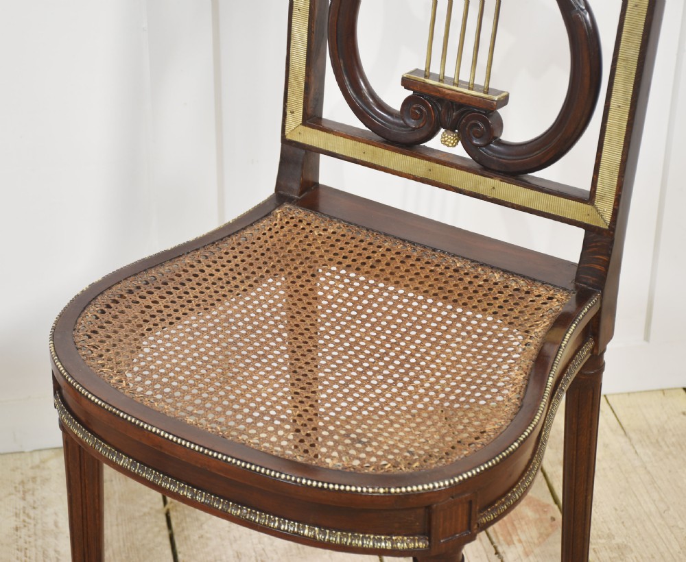 A pair of antique mahogany side chairs featuring open lyre-shaped backrests with brass accents and blue fabric seats upholstered with floral tapestry. View IX