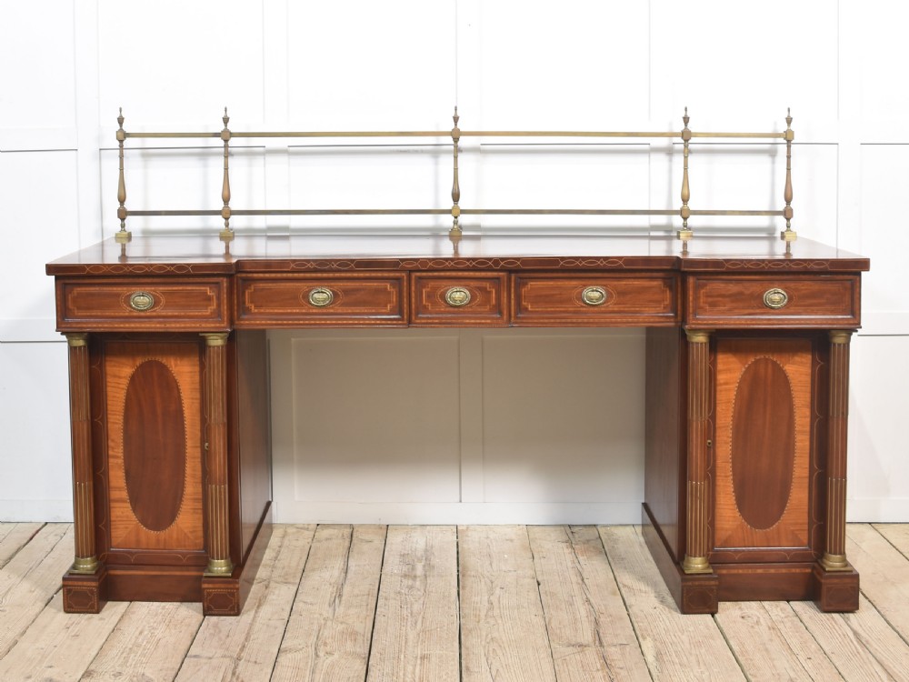 A 19th-century mahogany pedestal sideboard with satinwood oval panel inlays, reeded columns, five upper drawers, and a top brass gallery rail.