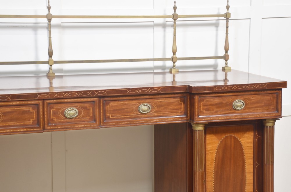 A 19th-century mahogany pedestal sideboard with satinwood oval panel inlays, reeded columns, five upper drawers, and a top brass gallery rail. View II