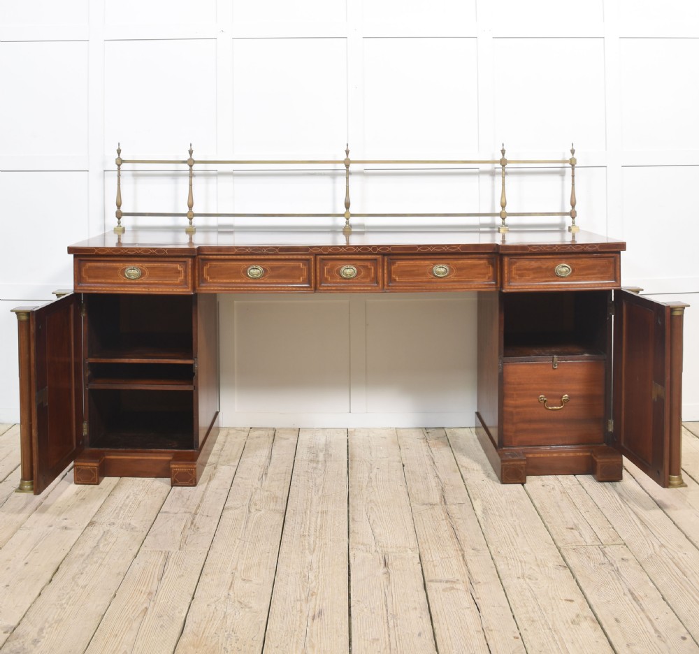 A 19th-century mahogany pedestal sideboard with satinwood oval panel inlays, reeded columns, five upper drawers, and a top brass gallery rail. View VII
