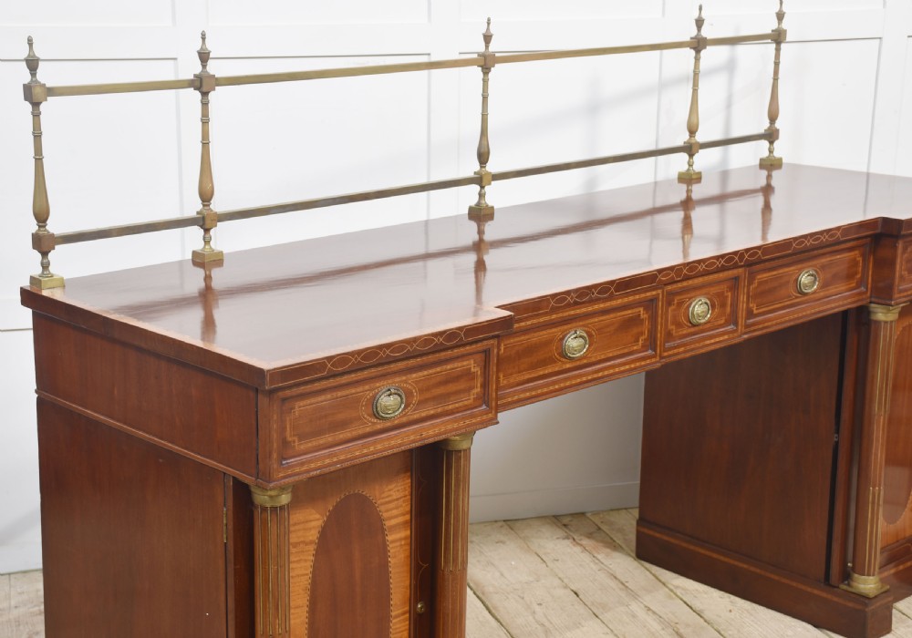 A 19th-century mahogany pedestal sideboard with satinwood oval panel inlays, reeded columns, five upper drawers, and a top brass gallery rail. View X