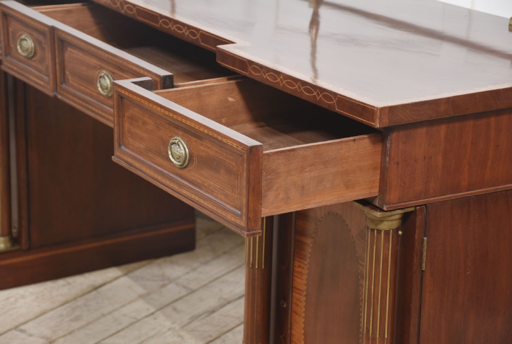 A 19th-century mahogany pedestal sideboard with satinwood oval panel inlays, reeded columns, five upper drawers, and a top brass gallery rail. View XIV