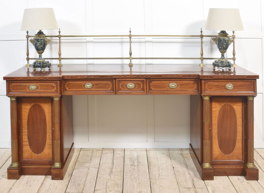 A 19th-century mahogany pedestal sideboard with satinwood oval panel inlays, reeded columns, five upper drawers, and a top brass gallery rail. View XVI