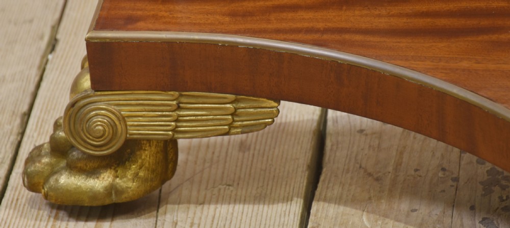A circular mahogany coffee table featuring a polished flame mahogany veneer top, a thin brass gallery rim, and four curved legs ending in brass lion paw feet. View III
