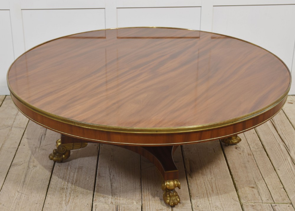 A circular mahogany coffee table featuring a polished flame mahogany veneer top, a thin brass gallery rim, and four curved legs ending in brass lion paw feet. View V