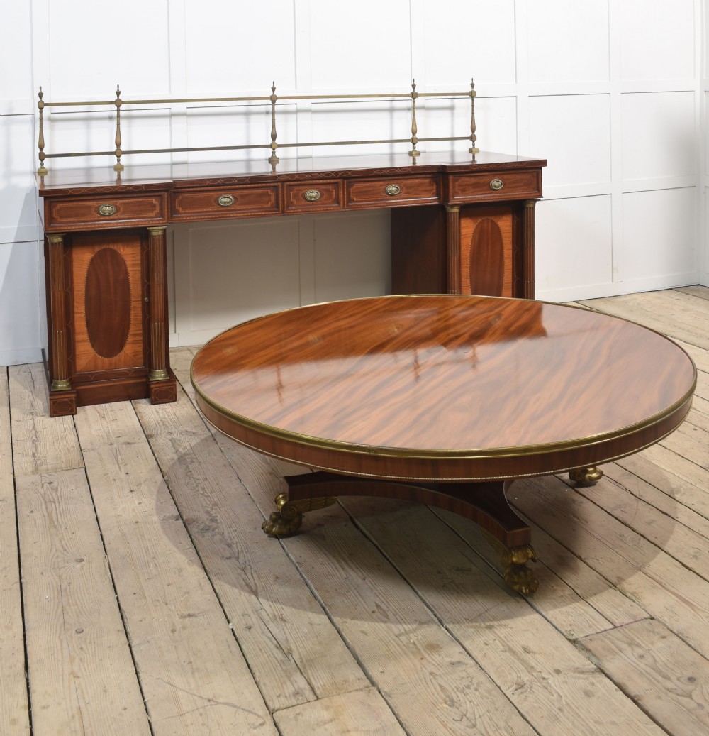 A circular mahogany coffee table featuring a polished flame mahogany veneer top, a thin brass gallery rim, and four curved legs ending in brass lion paw feet. View VI