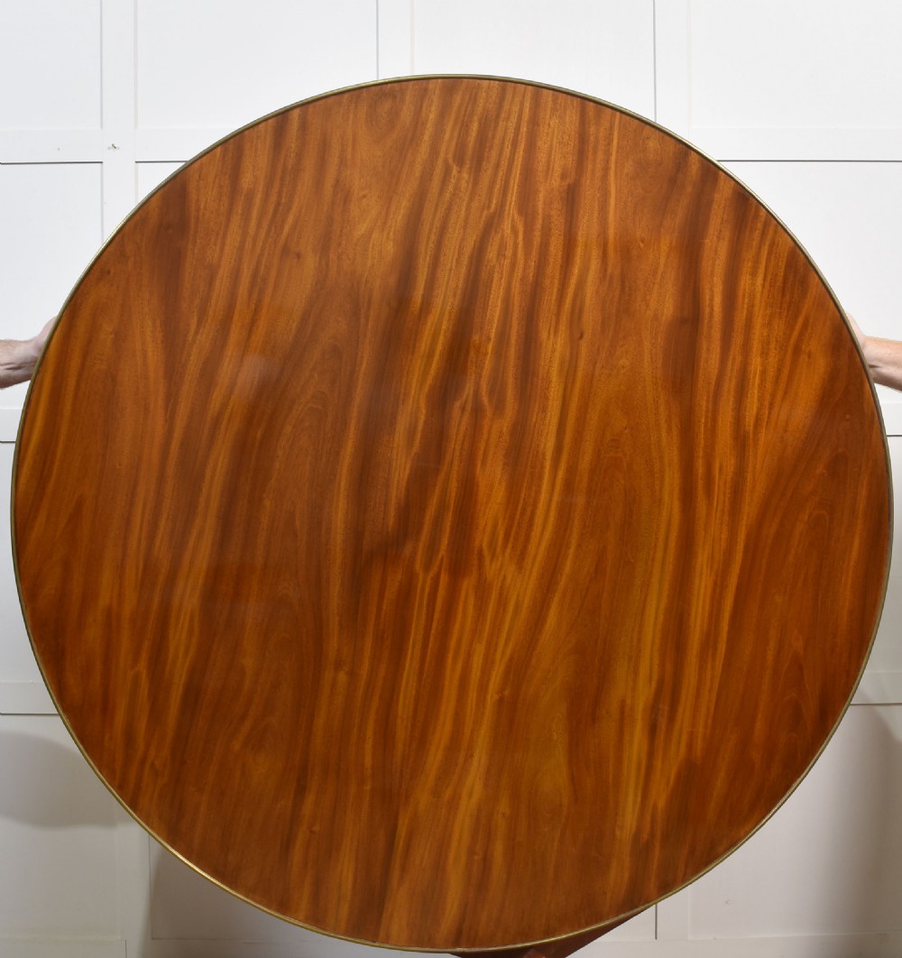 A circular mahogany coffee table featuring a polished flame mahogany veneer top, a thin brass gallery rim, and four curved legs ending in brass lion paw feet. View VIII