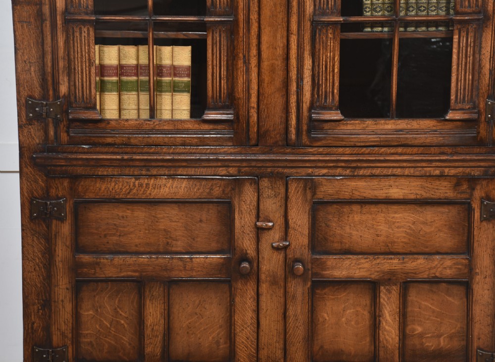 A tall dark oak two-door glazed bookcase featuring carved arched upper sections and panelled cupboard doors below. View VIII