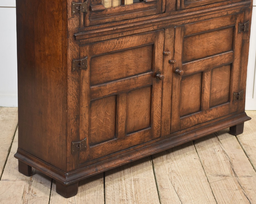 A tall dark oak two-door glazed bookcase featuring carved arched upper sections and panelled cupboard doors below. View IX