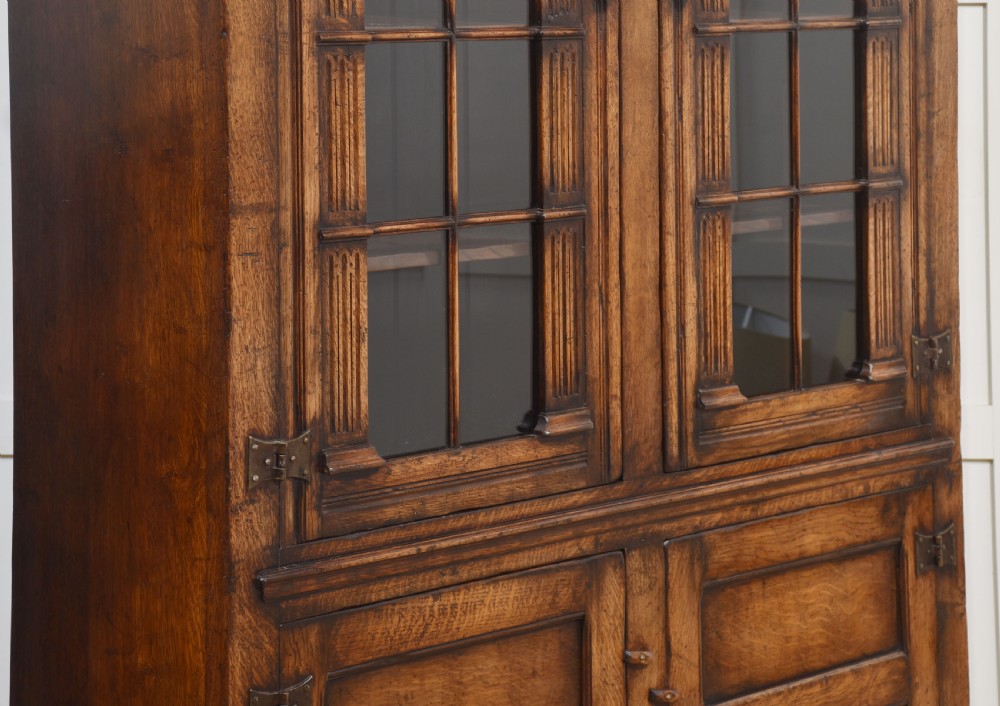 A tall dark oak two-door glazed bookcase featuring carved arched upper sections and panelled cupboard doors below. View XII