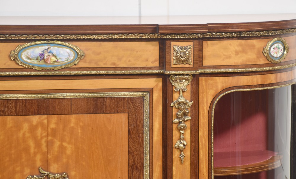 A 19th-century satinwood credenza featuring curved glass side display doors, a central solid panel door set with a porcelain plaque, and gilded ormolu mounts throughout. View III