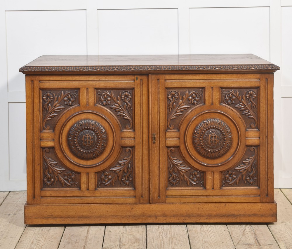 A 19th-century carved oak low cabinet featuring two door panels adorned with central carved roundels and foliate motifs.