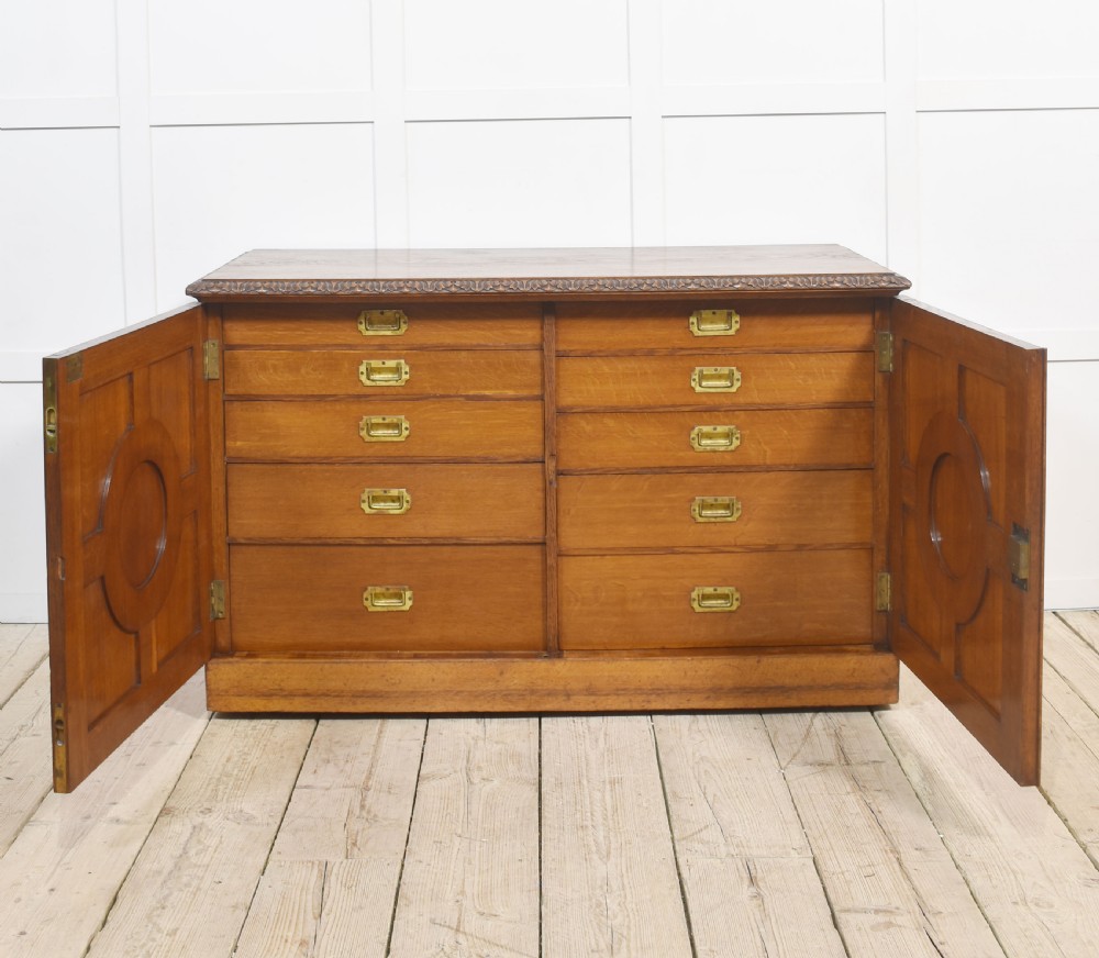A 19th-century carved oak low cabinet featuring two door panels adorned with central carved roundels and foliate motifs. View VI