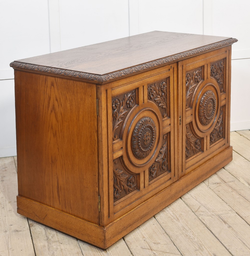 A 19th-century carved oak low cabinet featuring two door panels adorned with central carved roundels and foliate motifs. View IX