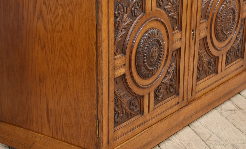 A 19th-century carved oak low cabinet featuring two door panels adorned with central carved roundels and foliate motifs. View X