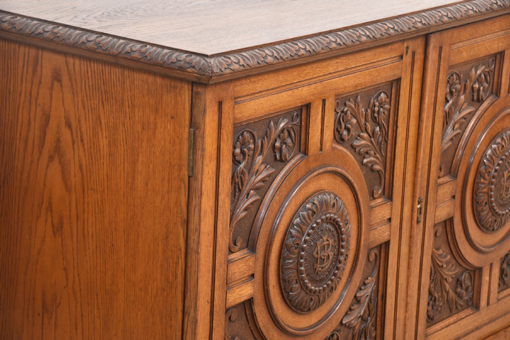 A 19th-century carved oak low cabinet featuring two door panels adorned with central carved roundels and foliate motifs. View XI