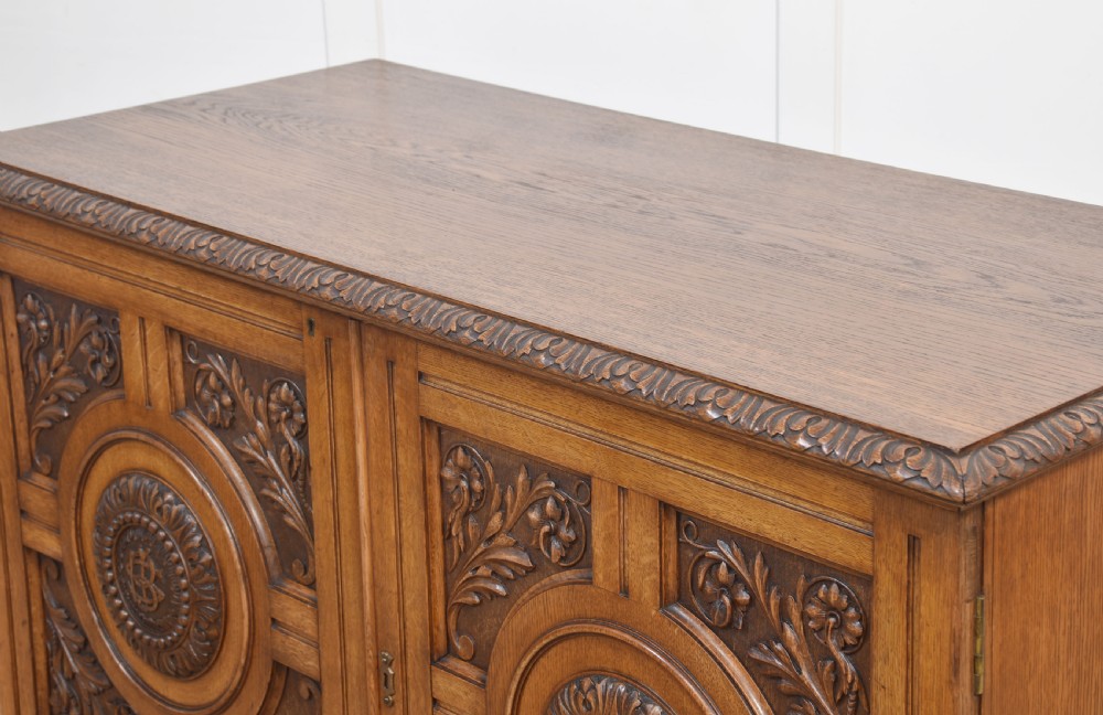 A 19th-century carved oak low cabinet featuring two door panels adorned with central carved roundels and foliate motifs. View XV
