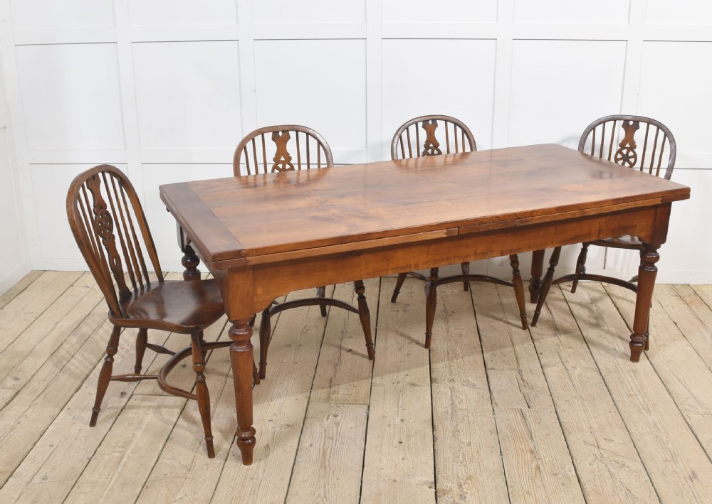 A large antique fruitwood farmhouse dining table featuring a smooth planked top, straight apron, and four turned legs resting on exposed wooden floorboards. View VI