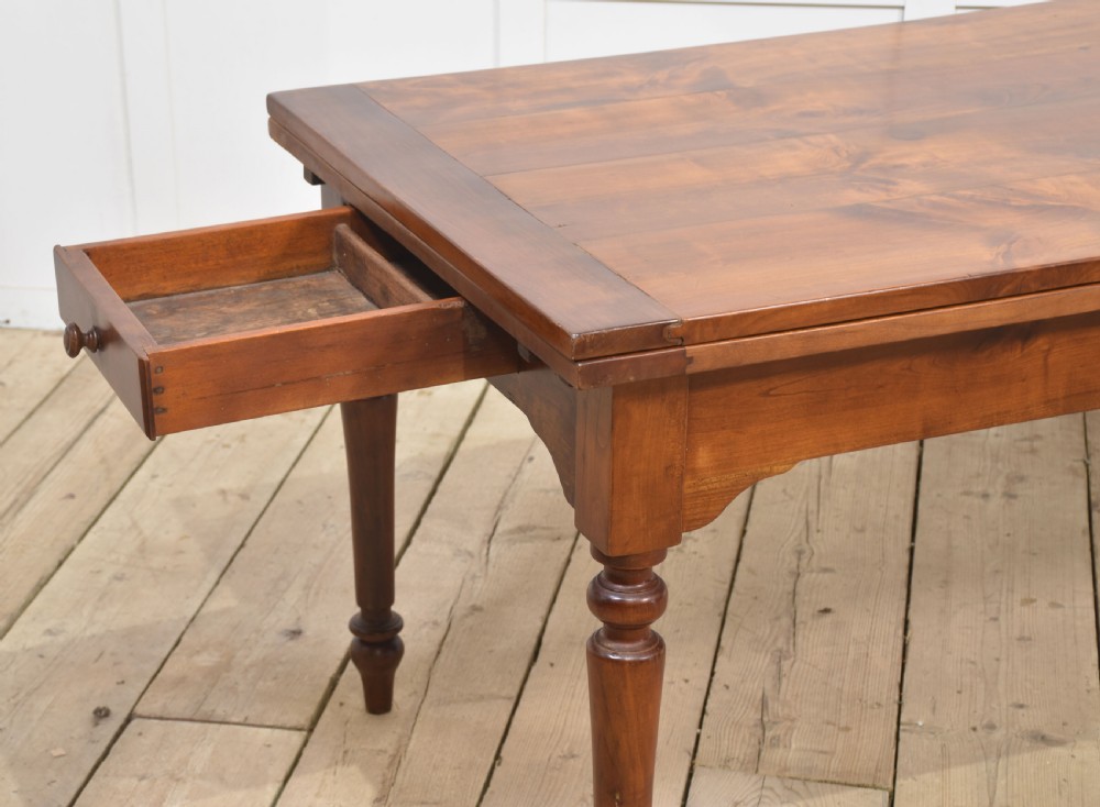 A large antique fruitwood farmhouse dining table featuring a smooth planked top, straight apron, and four turned legs resting on exposed wooden floorboards. View VII