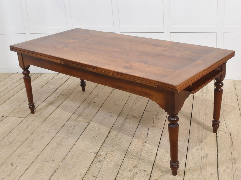 A large antique fruitwood farmhouse dining table featuring a smooth planked top, straight apron, and four turned legs resting on exposed wooden floorboards. View VIII