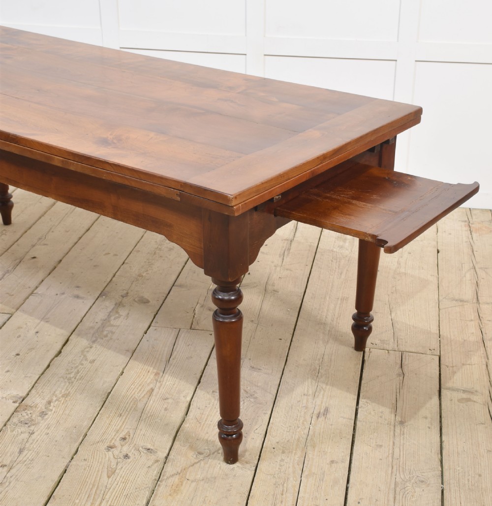 A large antique fruitwood farmhouse dining table featuring a smooth planked top, straight apron, and four turned legs resting on exposed wooden floorboards. View IX