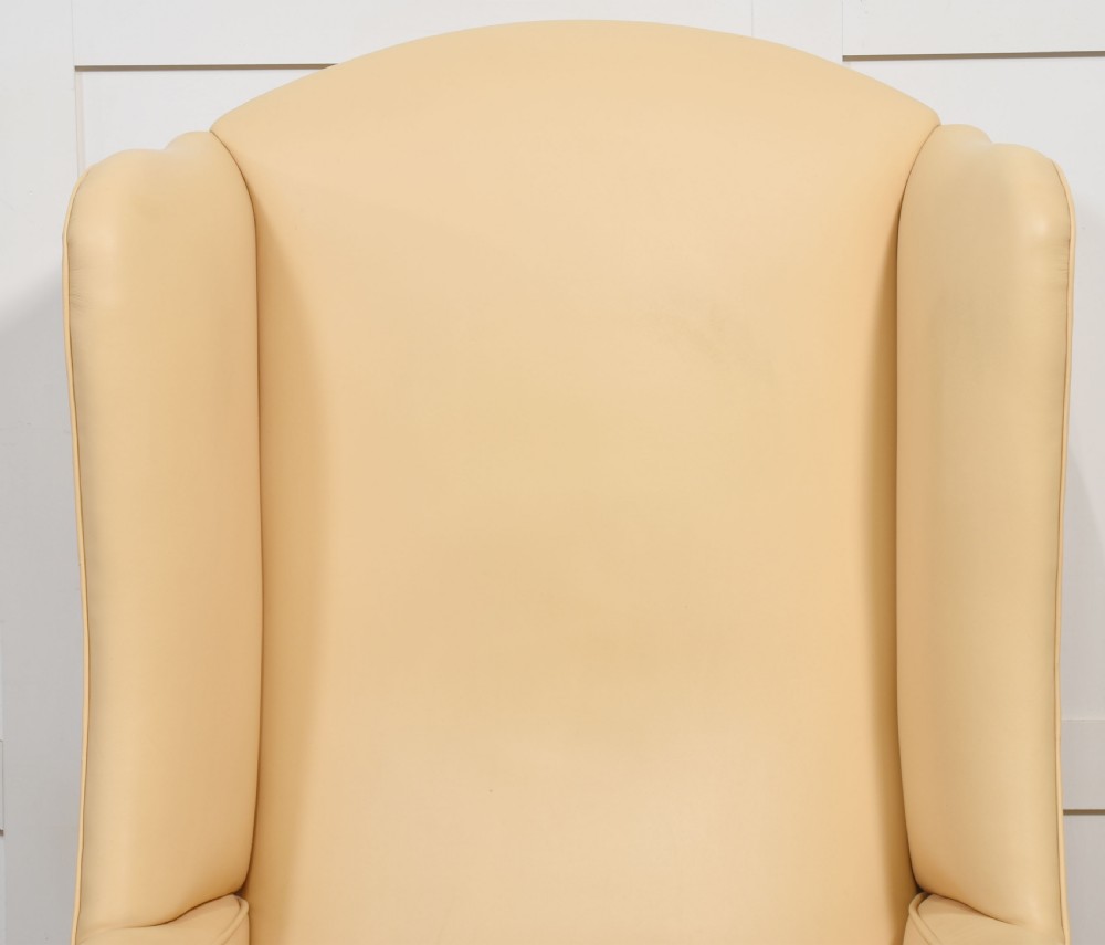 A high-backed cream leather wingback armchair with a fitted seat cushion and dark timber legs on brass castors. View V
