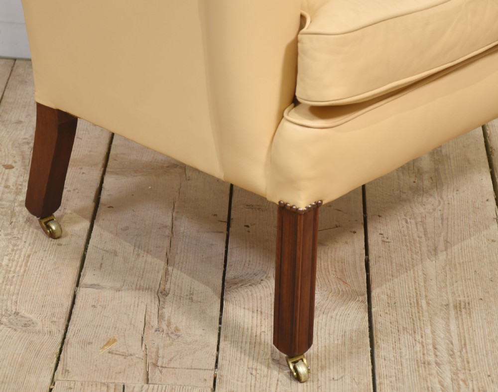 A high-backed cream leather wingback armchair with a fitted seat cushion and dark timber legs on brass castors. View VIII