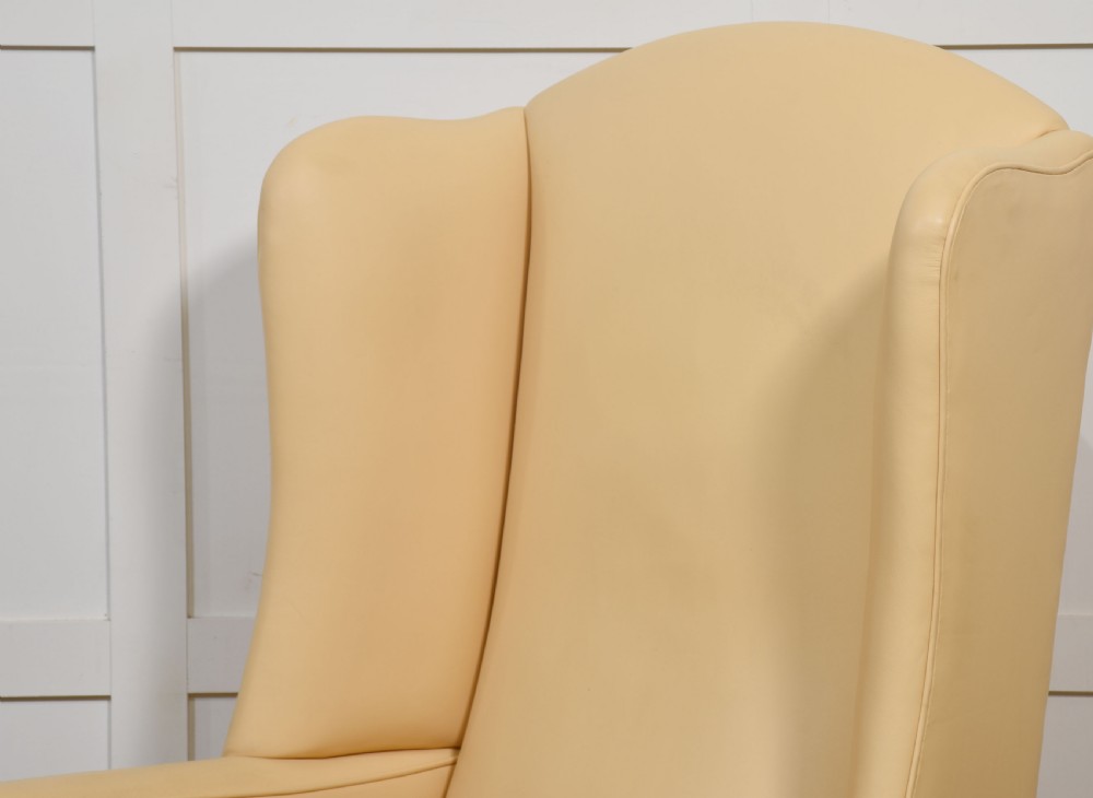 A high-backed cream leather wingback armchair with a fitted seat cushion and dark timber legs on brass castors. View XI