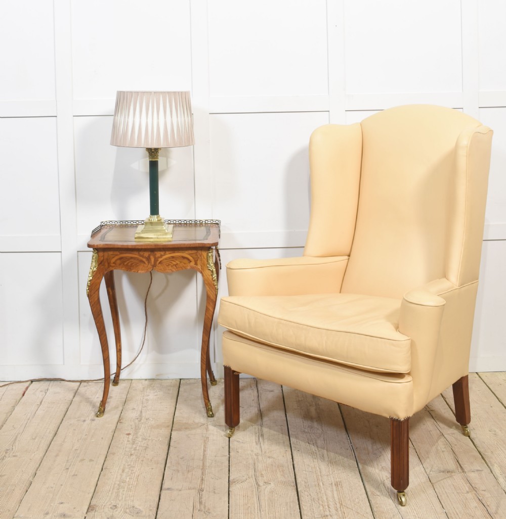 A high-backed cream leather wingback armchair with a fitted seat cushion and dark timber legs on brass castors. View XIII