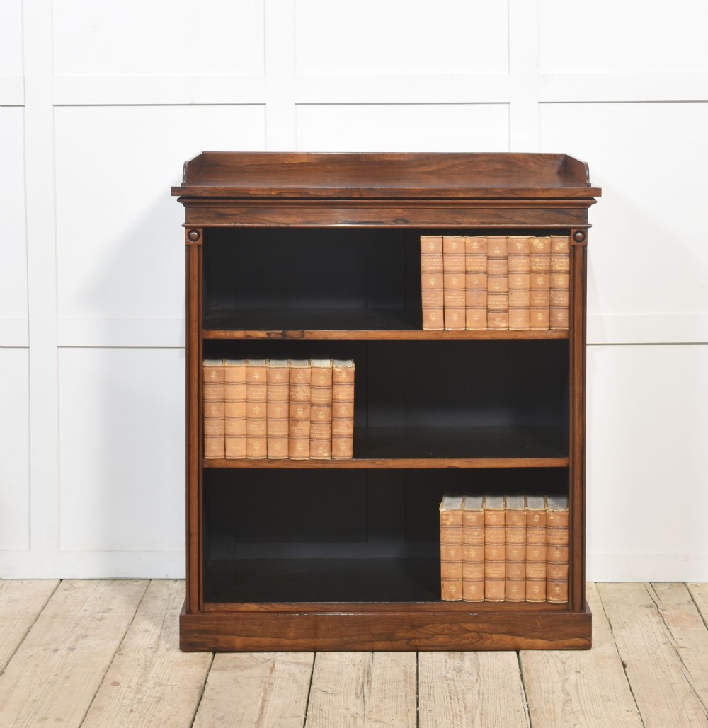 A 19th-century dark rosewood open bookcase featuring three tiers of shelving, a gallery top, corner roundels, and a solid plinth base.