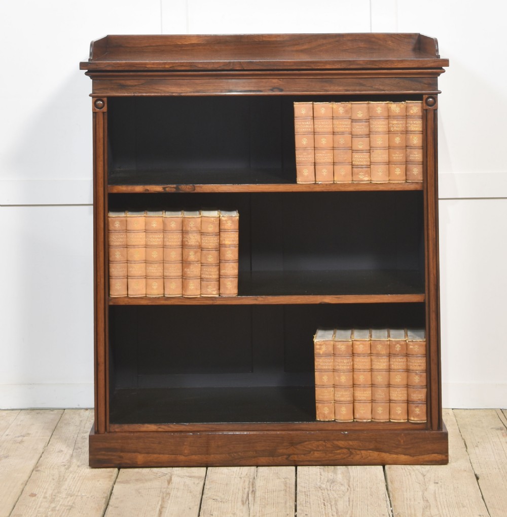 A 19th-century dark rosewood open bookcase featuring three tiers of shelving, a gallery top, corner roundels, and a solid plinth base. View VI
