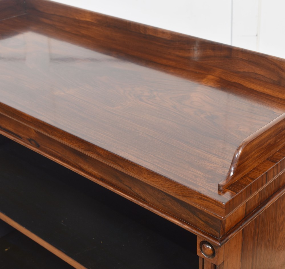 A 19th-century dark rosewood open bookcase featuring three tiers of shelving, a gallery top, corner roundels, and a solid plinth base. View XI