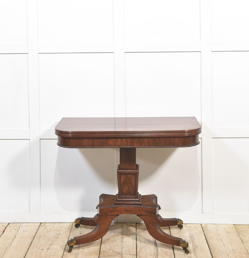 A Regency mahogany tea table featuring a fold-over top, central pedestal support, and four splayed legs with brass paw castors.