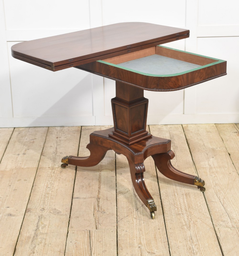 A Regency mahogany tea table featuring a fold-over top, central pedestal support, and four splayed legs with brass paw castors. View II