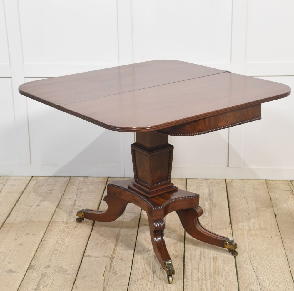 A Regency mahogany tea table featuring a fold-over top, central pedestal support, and four splayed legs with brass paw castors. View III