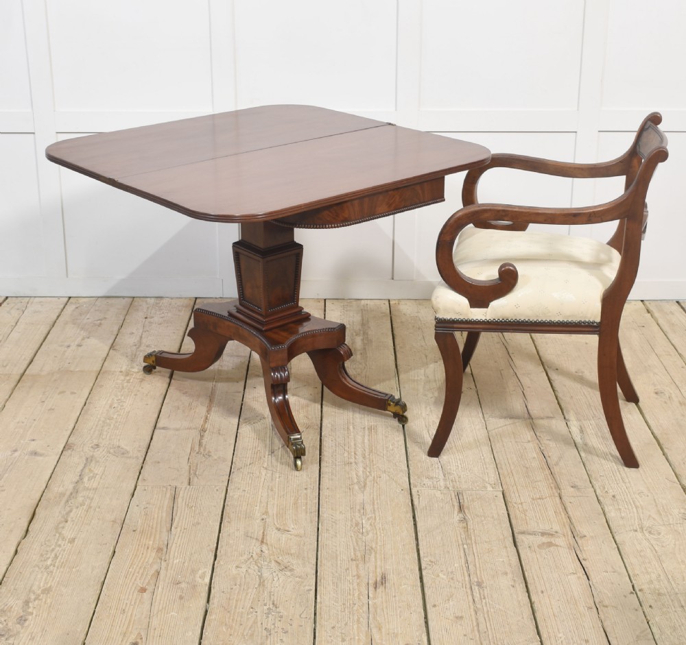 A Regency mahogany tea table featuring a fold-over top, central pedestal support, and four splayed legs with brass paw castors. View V